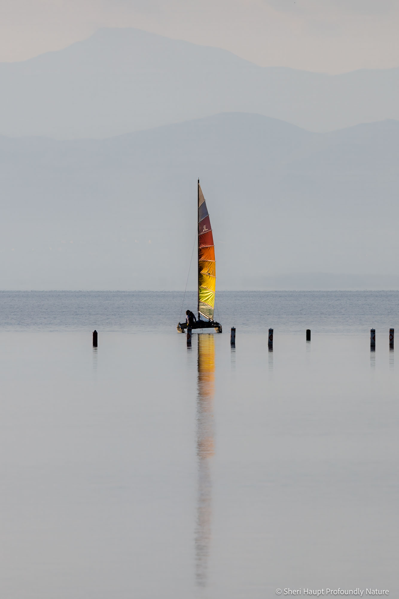 Quiet Passage A lone sail drifts across calm water, its reflection stretching into stillness. Soft layers of distant mountains fade into one...